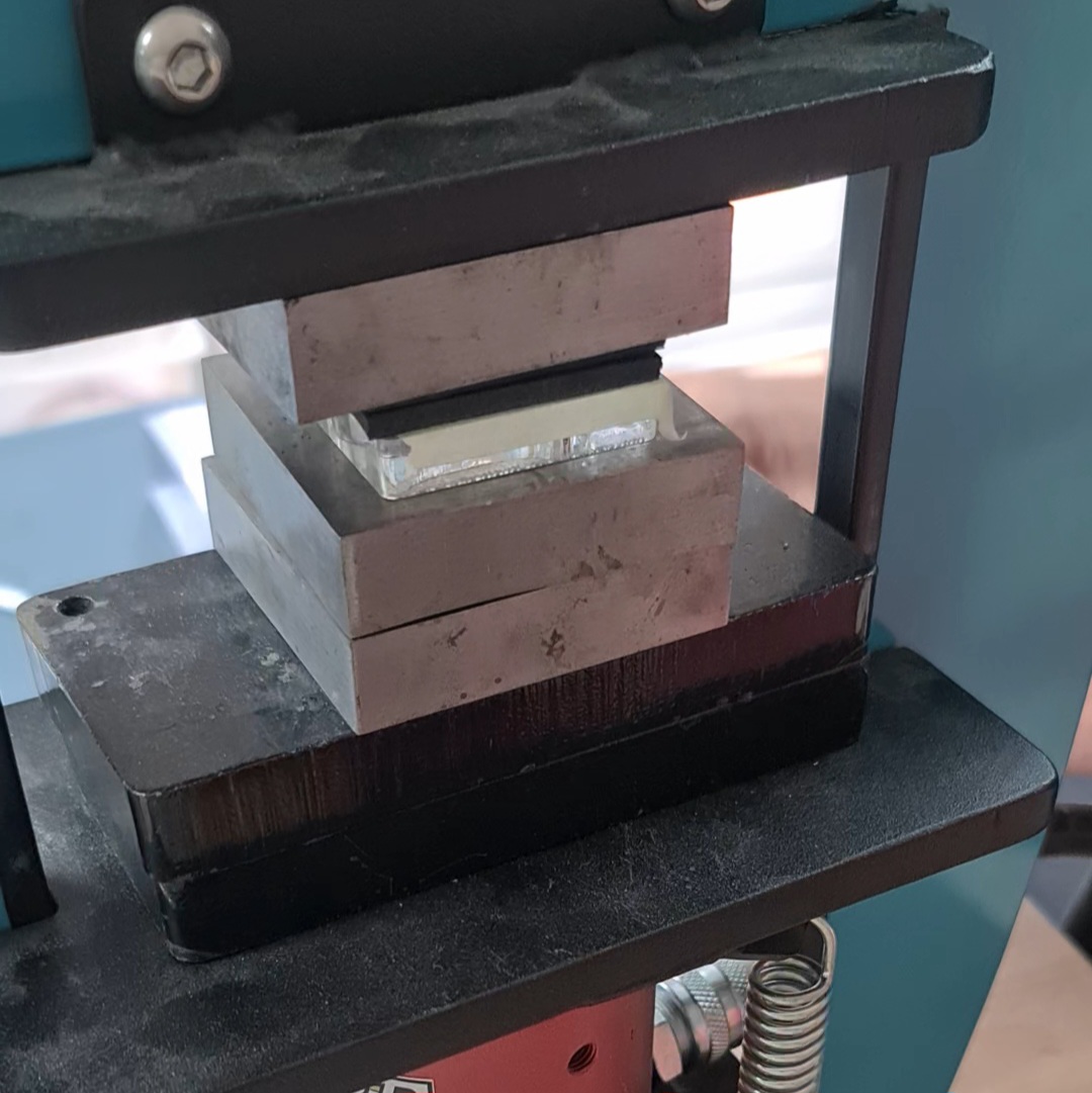 image shows silhouette die, silver, rubber sheets and metal block under the hydraulic press